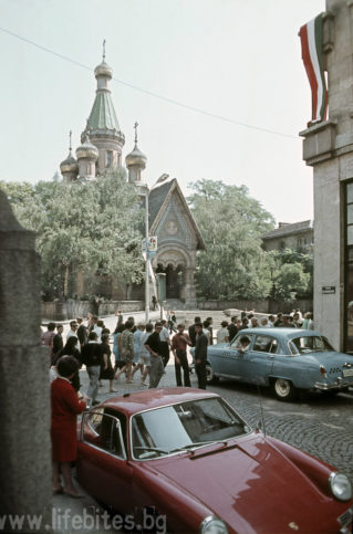 София, лятото на 1968 г. Минувачи зяпат червено порше, паркирано на столичната улица Бенковски. На заден план се вижда един от хилядите транспаранти, с които е окичен града по време на Младежкия фестивал.