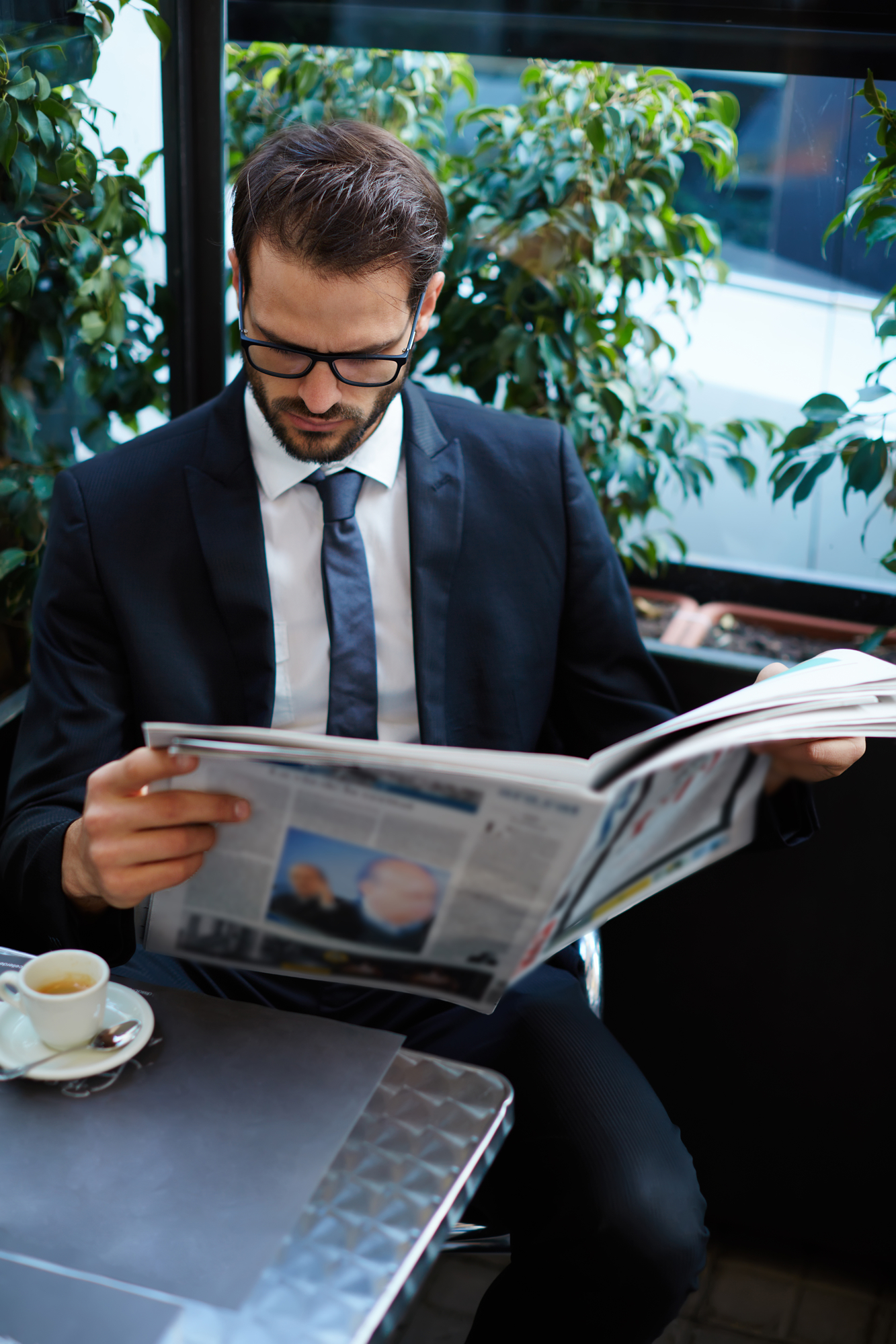 Portrait of young brunette hair businessman sitting in a coffee shop reading a newspaper looking concentrated, handsome business man holding open newspaper sitting in cafe